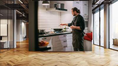 A male cook is cooking at the stove at home in the kitchen Wall mural