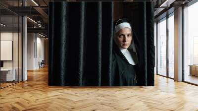 A serious-looking nun in traditional black habit and white wimple stands behind a black curtain, gazing intensely off-screen, captured in a dramatic moment Wall mural