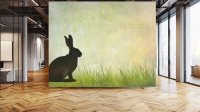 A silhouette of a rabbit sitting amidst grass in a natural landscape Wall mural