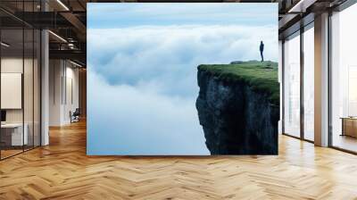 A solitary figure stands at the edge of a rugged cliff, surrounded by vast clouds that create a peaceful atmosphere during the early morning, evoking a sense of tranquility and reflection Wall mural