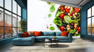 A vibrant bowl of fresh salad featuring spinach, cherry tomatoes, chickpeas, and black olives, garnished with spices, ideal for a nutritious and delicious meal Wall mural