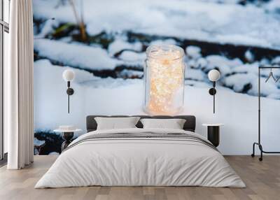 A vintage glass jar with a garland inside stands on a snow-covered sleeper on an abandoned railway covered with snow. Winter holiday concept. Close up Wall mural