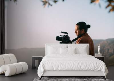 A young Caucasian man with a professional camera in his hands on a mountain by the sea. Wall mural