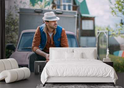 A young farmer in work clothes sits on a shovel with a small truck. The concept of delivery of agricultural products and small busines Wall mural