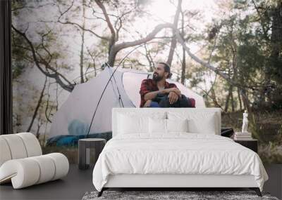 A young man with a hiking backpack near a tent in a tourist camp. Wall mural