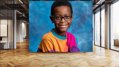 An African American teenage boy wearing glasses and a colorful t-shirt sits against a light blue background. Wall mural