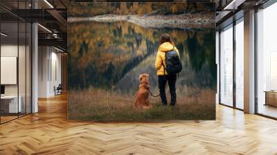 Traveling with the dog. A girl and a dog stand by a mountain lake in autumn.  Wall mural