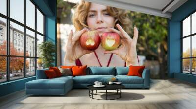 beautiful young woman 18 - 20 years old holds in hand two apples with hearts carved into them. focus on apples. Proper vitamin nutrition, diet. Surprise for loved one. healthy eating and lifestyle Wall mural