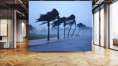 Bending palm trees line a waterfront pathway as strong winds and rain cause turbulent waves in the early evening, creating a dramatic and moody atmosphere Wall mural