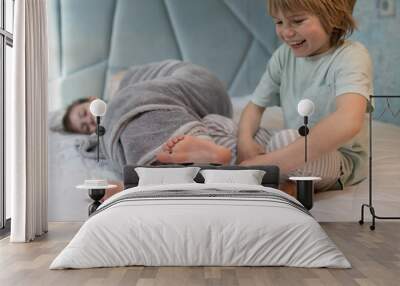 cute children in pajamas play around on the bed at home. brother tickles sister's bare feet. Cheerful childhood of offspring, pampering at home, cozy rest. selective focus Wall mural