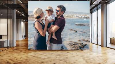 Family with a child stand on the stones against the background of the sea. Wall mural