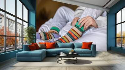 A woman in warm pants putting on a second pair of warm socks to keep warm in the winter without heating, energy and economic crisis concept Wall mural