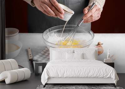 Woman pour milk into a bowl of beaten eggs and flour, mix with whisk on a gray table in the kitchen. Authentic female hands making a dough for homemade pie, Home baking concept, pie crust recipe Wall mural