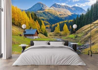 Golden trees surround a rustic cabin by a sparkling stream, with majestic mountains rising in the background under clear skies in a stunning autumn setting Wall mural