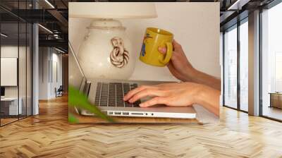 Green space in everyday life: working on laptop, drinking coffee,  stylish home office oasis. Woman with a yellow coffee mug typing on keyboard, working remotely freelance. Differential focus. Wall mural