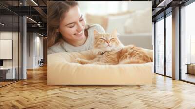 Happy young woman smiling at a content cat lounging in a cozy home setting Wall mural