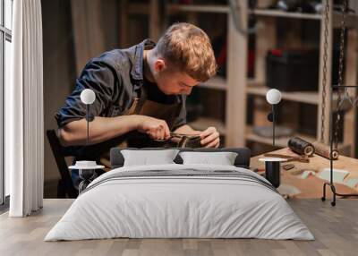 a young man is engaged in the family craft of making leather shoes in a workshop Wall mural