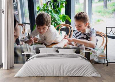 Two kids with their mother sharing food at dinner Wall mural