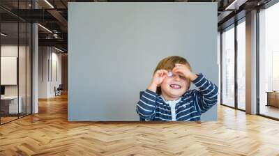 Little boy  wearing striped t shirt sitting at the table, learning at home during coronavirus quarantine. Toddler playing with shaped stickers. Early development. Copy space on the left. Wall mural