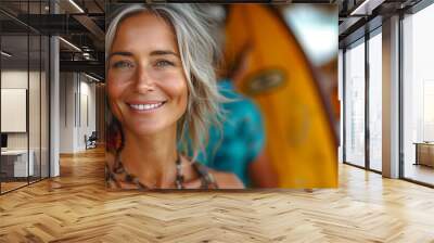 A portrait of a beautiful smiling middle-aged blonde woman standing with a surfboard on the beach Wall mural