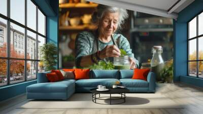 An elderly woman preparing a fresh green smoothie from herbs and vegetables in her kitchen at home. Healthy lifestyle, active aging, and home cooking concept. Wall mural