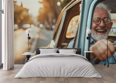 Happy laughing senior man riding a vintage car with a sunny street on a background. Active senior people concept. Wall mural