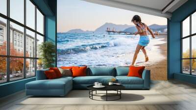 Little girl having fun at the beach, splashing in the water and waves, enjoying a relaxing leisure activity Wall mural