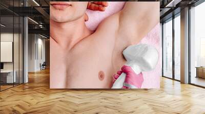 Male inflated body. A man in a beauty salon undergoes laser hair removal in the armpit area. Male body care. The master in pink gloves holds the head of the device during the procedure Wall mural