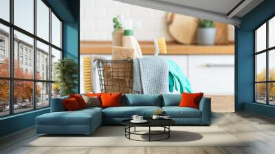 Basket with brushes, rags, natural sponges and cleaning products. Modern kitchen interior in the background. House cleaning concept Wall mural