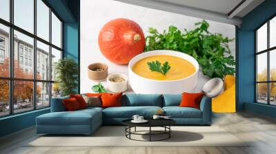 Pumpkin soup in bowl on light background surrounded by fresh vegetables and green herbs. Seasonal traditional autumn cream soup. Healthy food concept Wall mural