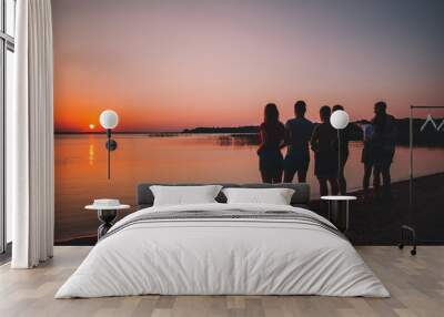 Silhouette of friends at the beach looking on the sunset in the summer evening Wall mural