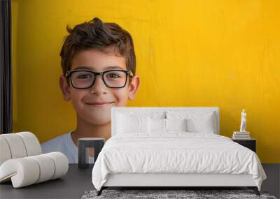 Smiling boy with glasses wearing a white t-shirt against a vibrant yellow background. Concepts of childhood, education, and happiness. Wall mural