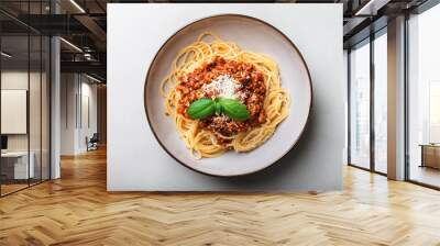 Spaghetti topped with a rich meat sauce, grated Parmesan, and fresh basil leaves, served on a round plate, viewed from above, placed on a light surface. Wall mural