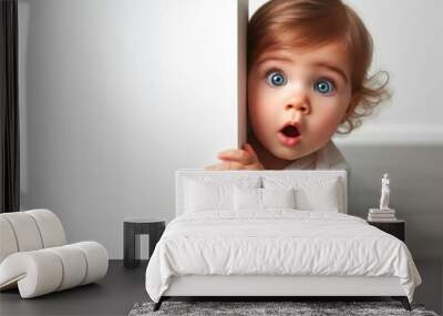 Surprised baby girl cautiously peeks around a corner against a white background Wall mural