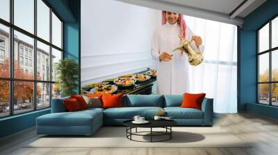 
Arab man in traditional white clothes pour tea on Iftar and eat Arab sweets Wall mural