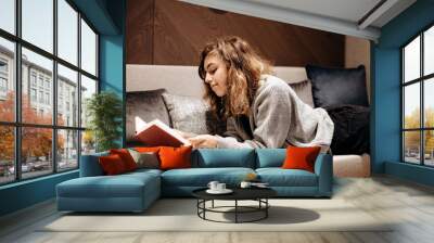 Teenager girl reading book on the couch at home Wall mural