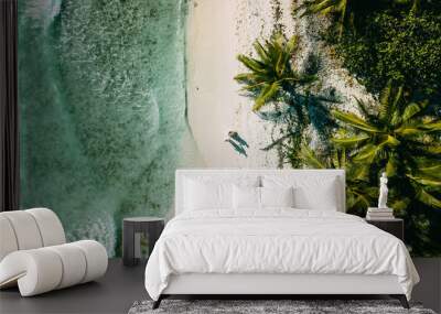 The couple walks on the beach between the ocean and palm trees Wall mural