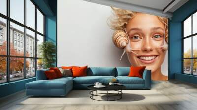 The woman beams with joy, showcasing a unique interaction as she playfully poses with two large snails on either side of her face, emphasizing her fun spirit and love for nature Wall mural