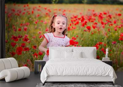 a little girl with blond hair in a bright dress with an ornament stands among a poppy field Wall mural