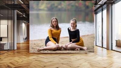 Two beautiful girl teenagers friends, sisters sitting on the beach front of the lake. Fall season. Family photography Wall mural