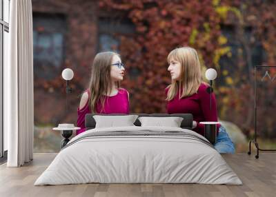 Two young teenager girls sitting on the rock, talking. Sisters, friends happy smiling, laughing, talking. Fall autumn time. Wall mural