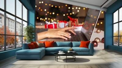 Christmas shopping online, sales and discounts promotions during winter holidays, online shopping at home and lockdown coronavirus. Female hands on the laptop with gifts and blurred bokeh lights Wall mural