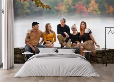 white Caucasian family sitting on a rocky wall, with the view on lake on fall. teenagers and parents.  Wall mural