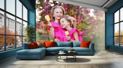 Happy kids eat ice cream. Portrait of two girls twin sisters hugging and laughing on background of bloom pink tree. Children summer vacation Wall mural