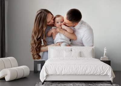 Happy young family. Beautiful Mother and father kissing their baby . Parents, Portrait of Mom, dad and smiling child on hands isolated over white background. Wall mural