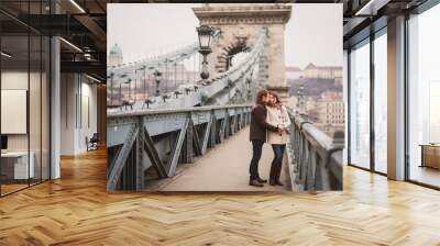 Christmas in old town. Young cheerful caucasian couple in warm cozy clothes walking in city centre. Wall mural