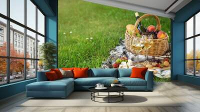 Picnic setting with  two glasses of white wine,  cheese, fruits and basket. Outdoor, green lawn Wall mural