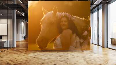 A young woman wearing a dress and her horse cuddling together during sunset in summer outdoors. Romantic horse and owner portrait Wall mural