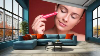 Beautiful brunette woman massage her face with a beauty massager. Her skin fresh, clean and flawless. Spa procedure concept Wall mural