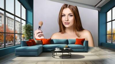 Beautiful red hair plus size model applying make up with a brush on a neutral grey background. Flawless skin, fashion glamour portrait Wall mural